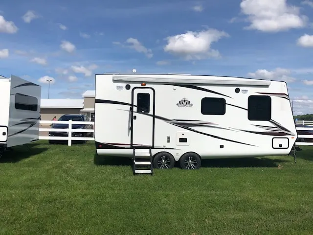 The white rental travel trailer parked on a grass site by the fence